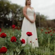 Woman in a white dress standing in a poppy field with red flowers in the foreground