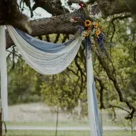 White draped fabric and a floral bouquet tied to a tree branch outdoors