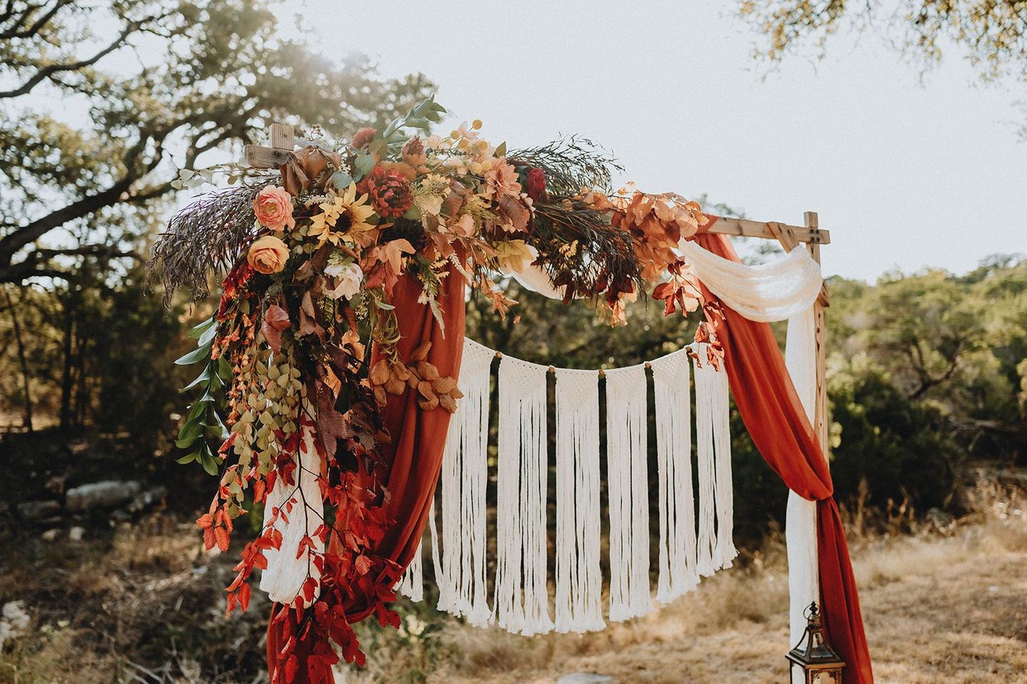 Floral wedding arch with red drapes and white ribbons outdoors in a rustic field