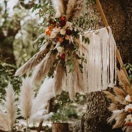 Boho floral arrangement with cream tassels and pampas grass hanging on a tree outdoors