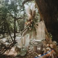 Outdoor floral altar with cream drapery, pampas grass, and white flowers in a wooded setting