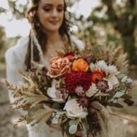 Woman holding a rustic bouquet of white, red, and orange flowers outdoors