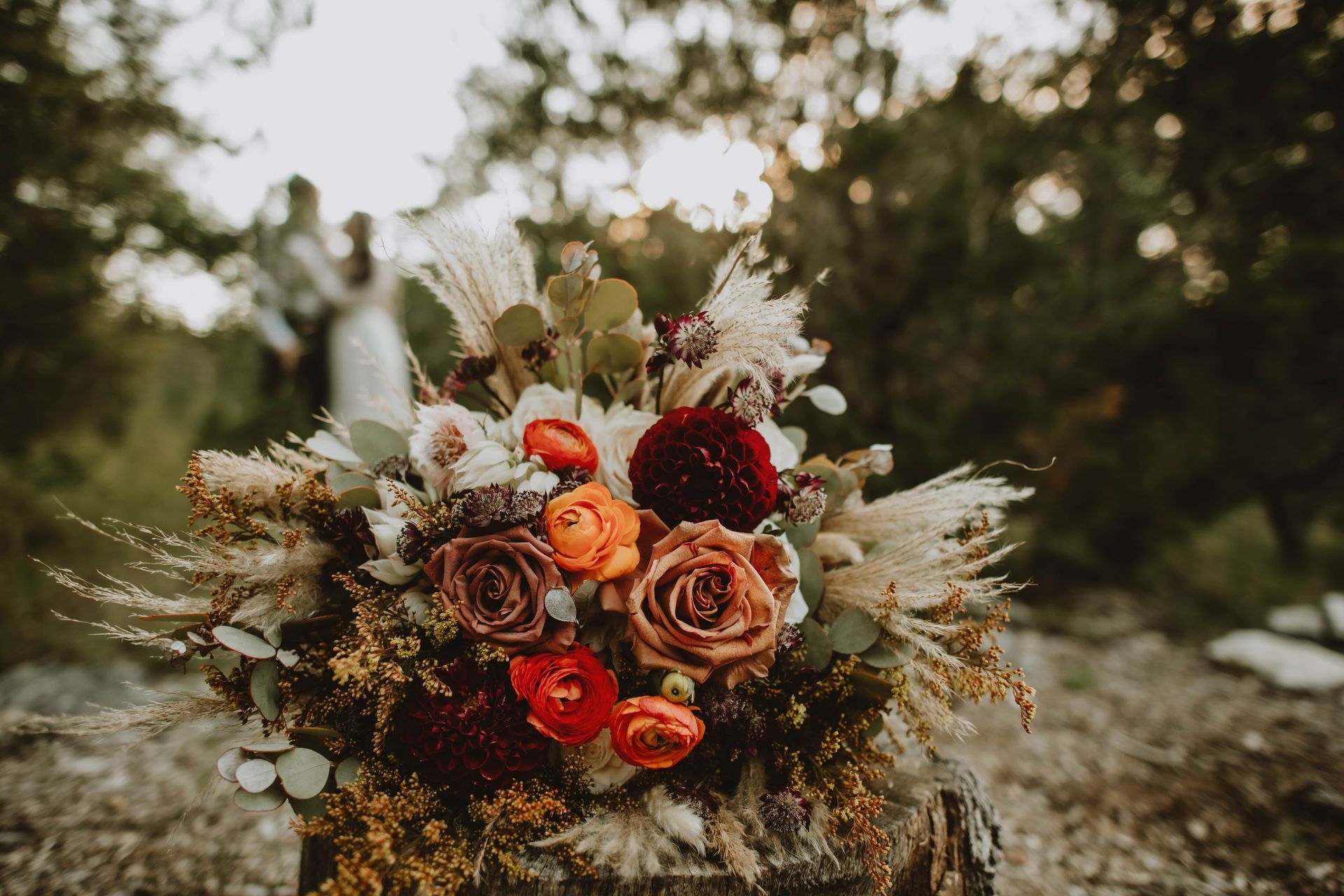 Autumn bouquet of orange, red, and cream flowers with dried grasses in an outdoor setting