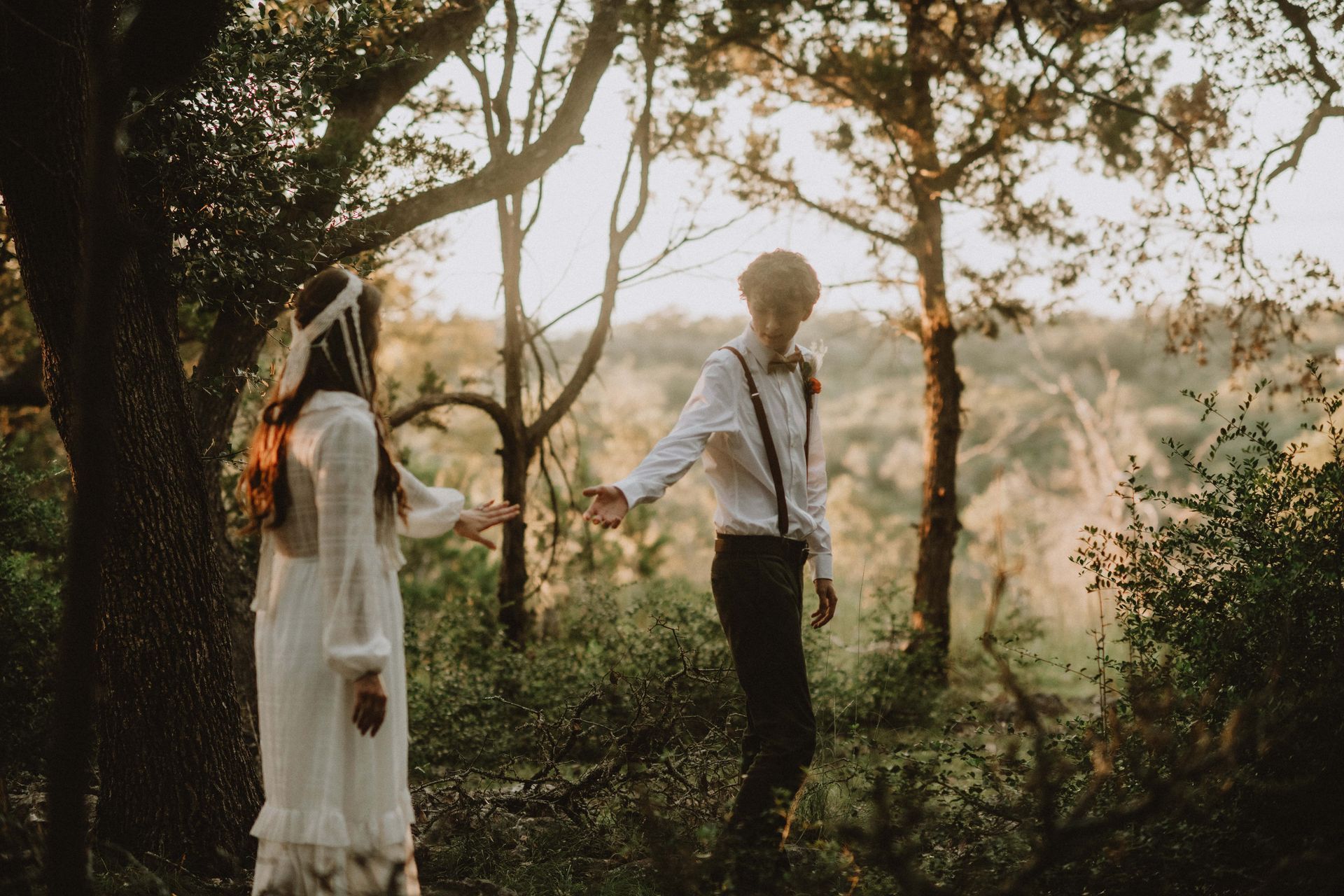 Two people in white outfits standing in a sunlit wooded clearing