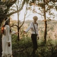 Two people in white shirts stand in a sunlit garden among trees and flowers