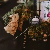 Candlelit altar with crystals, dried herbs, and a tarot card on a dark surface