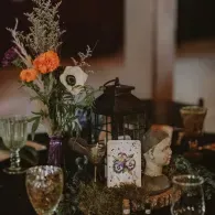 Decorative table with flowers, lantern, bust, and glassware in warm indoor lighting