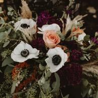 Bouquet of white, peach, and burgundy flowers with greenery in a dark setting