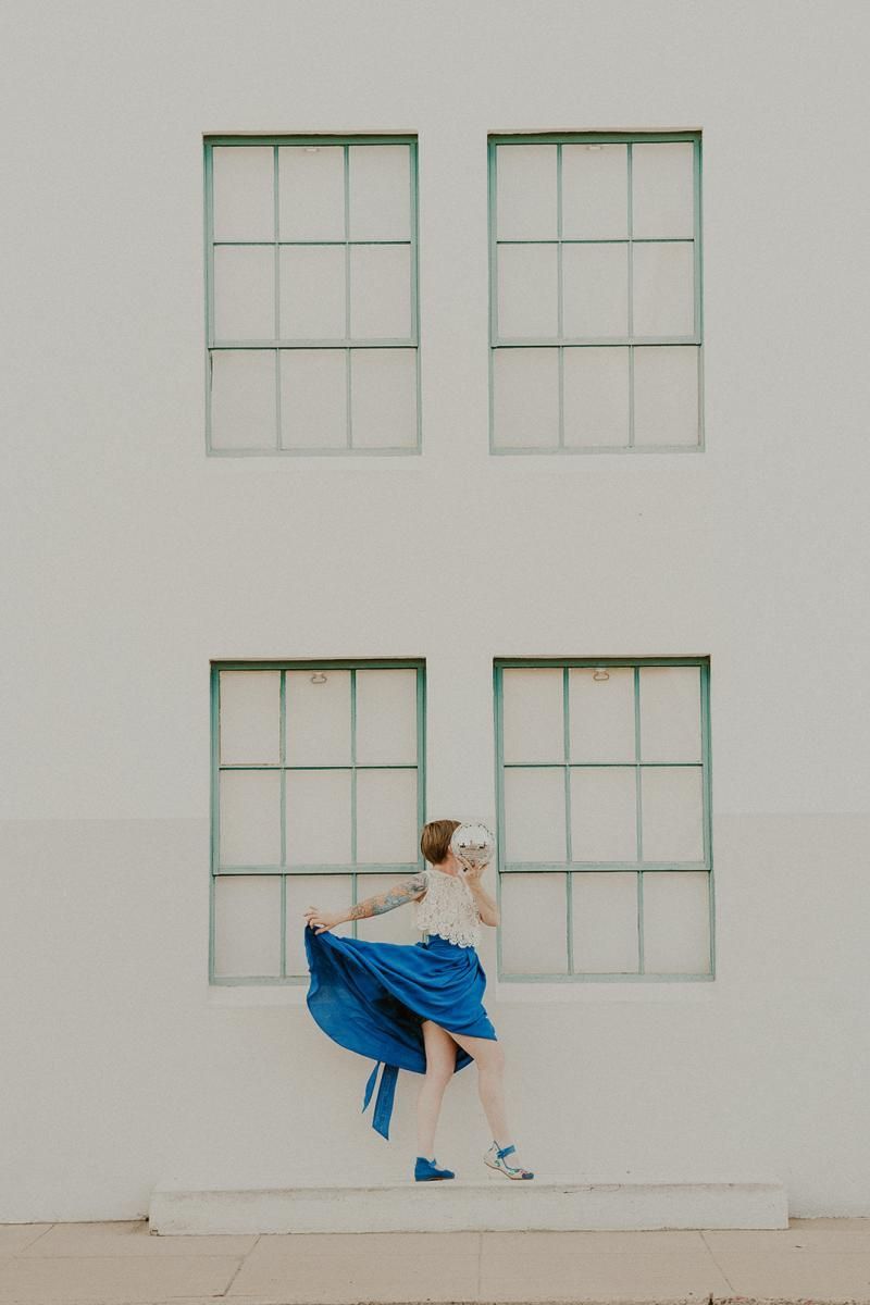 Dancer in a blue skirt mid-twirl in front of a white wall with four windows