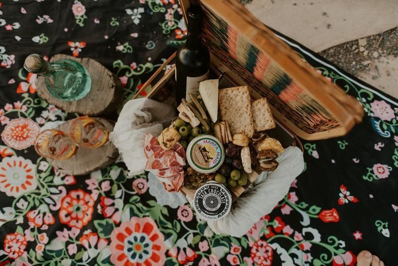 Assorted snacks and wine arranged on a floral tablecloth with a woven basket and decorative plates