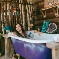 Woman relaxing in a purple-and-white bathtub in a rustic outdoor spa setting