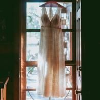 White dress hanging in a sunlit doorway with a window behind it