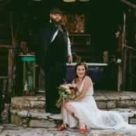 Bride sitting on stone steps with bouquet beside a groom at an outdoor rustic venue
