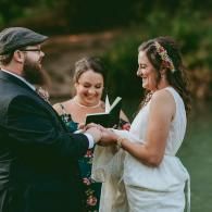 Couple exchanging vows outdoors while an officiant reads from a book