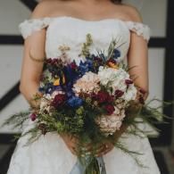 Woman in a white off-shoulder dress holding a colorful bouquet of wildflowers and greenery