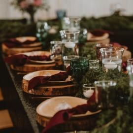 Set dining table with wooden plates, glassware, and burgundy napkins in a warm, dim setting