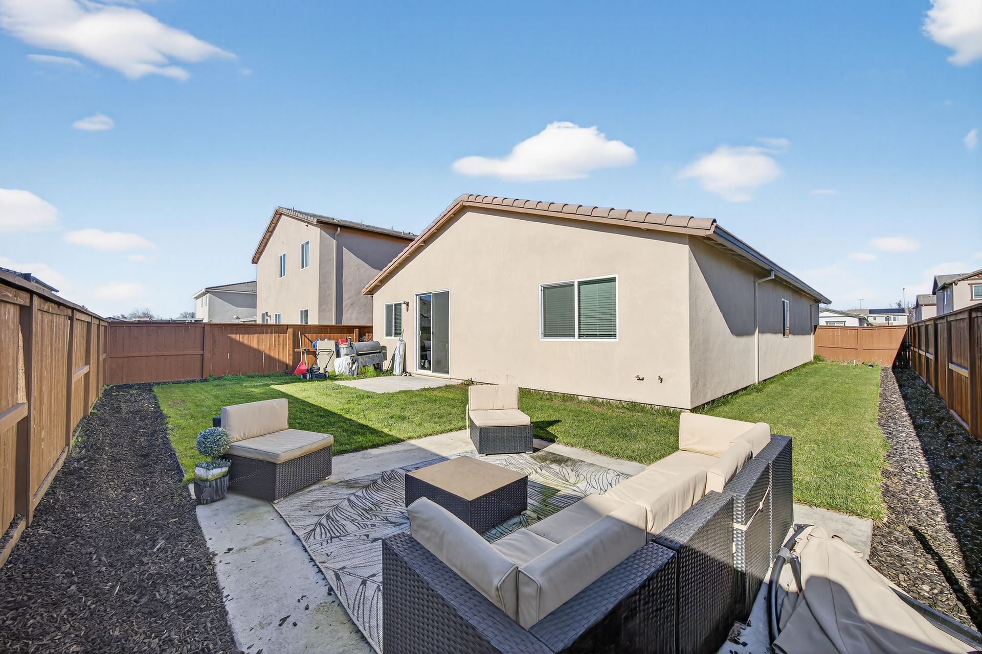 Backyard with patio furniture, green lawn, beige house, and wood fence.
