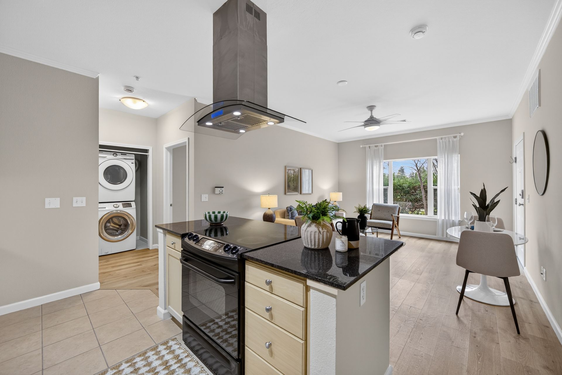 Open-concept kitchen and living area with island stove, laundry in the hall, and a view of the outdoors.