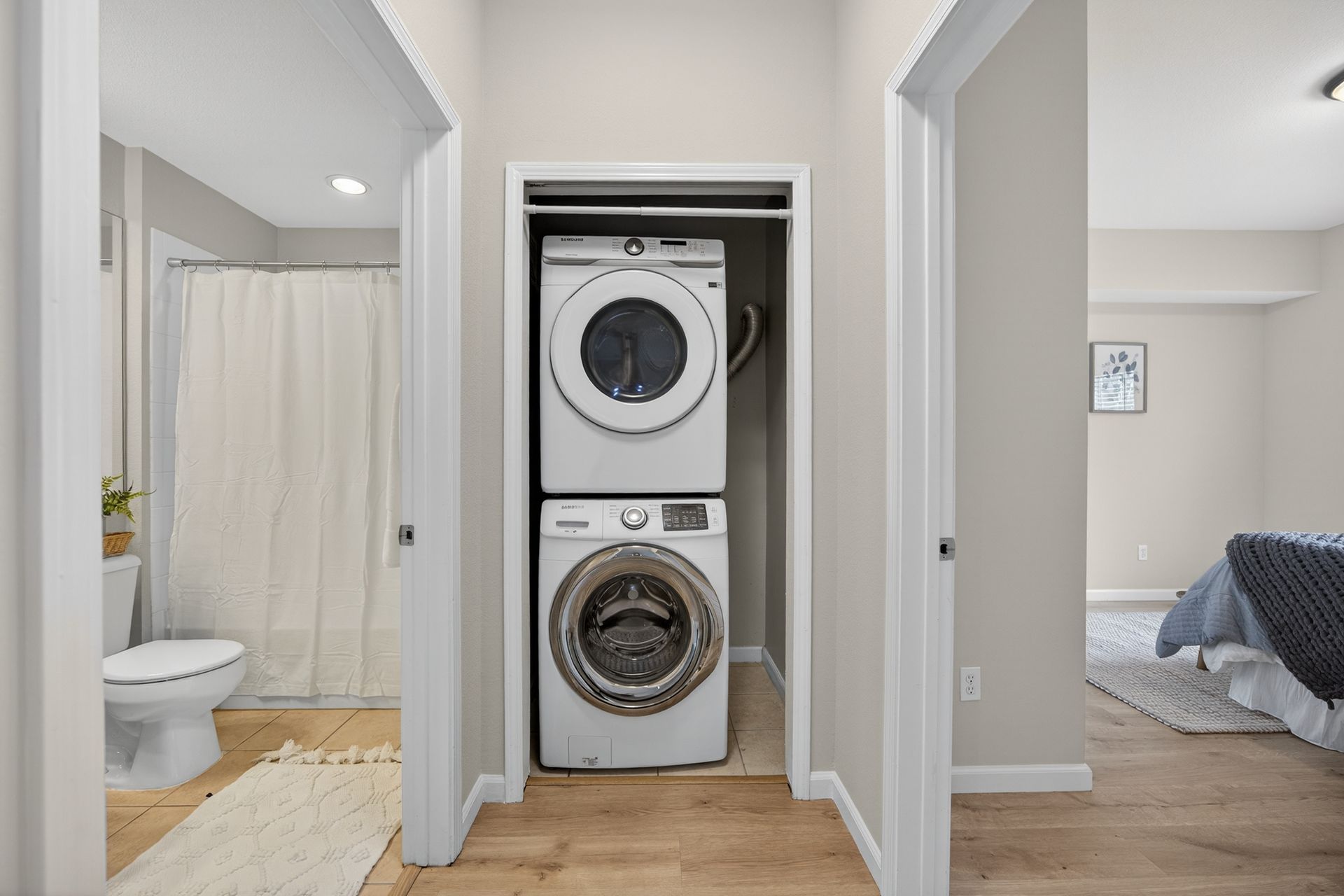 Laundry room with stacked washer and dryer between bathroom and bedroom doorways.