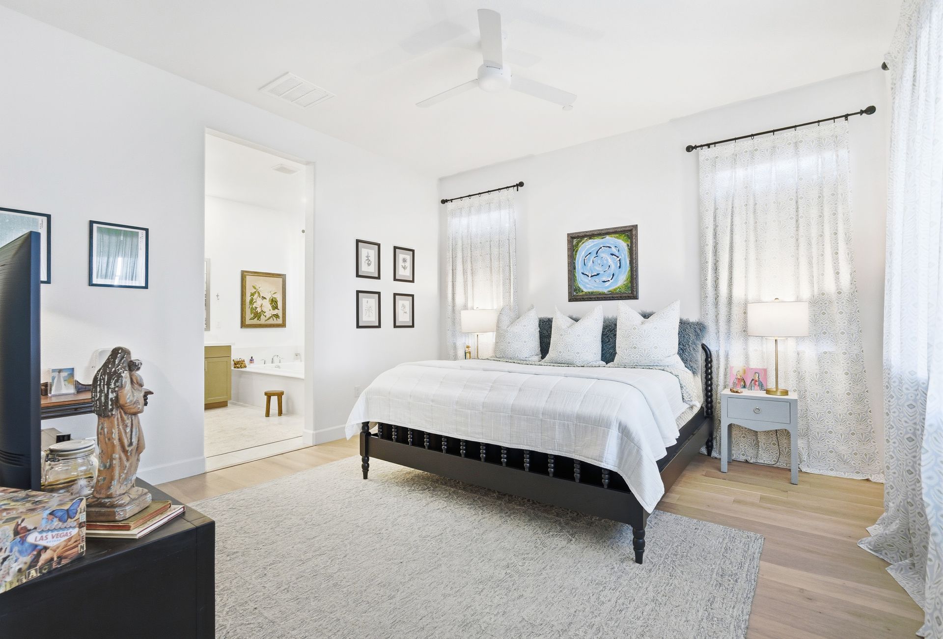 Bright bedroom with a black bed, white bedding, rug, and walls, with a hallway visible.