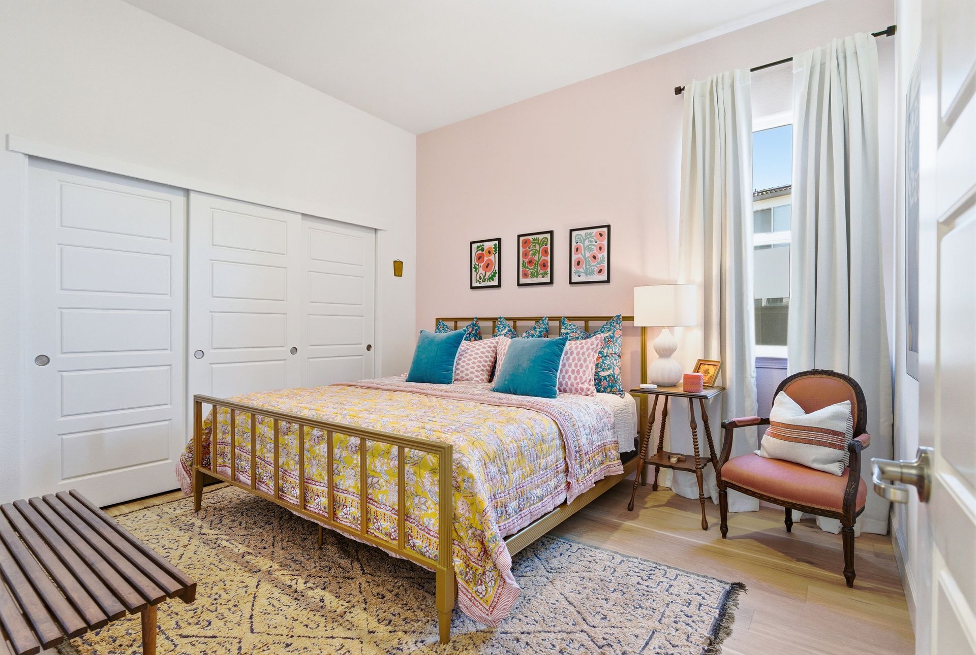 Bedroom with pink walls, gold bedframe, white curtains, and a patterned rug.