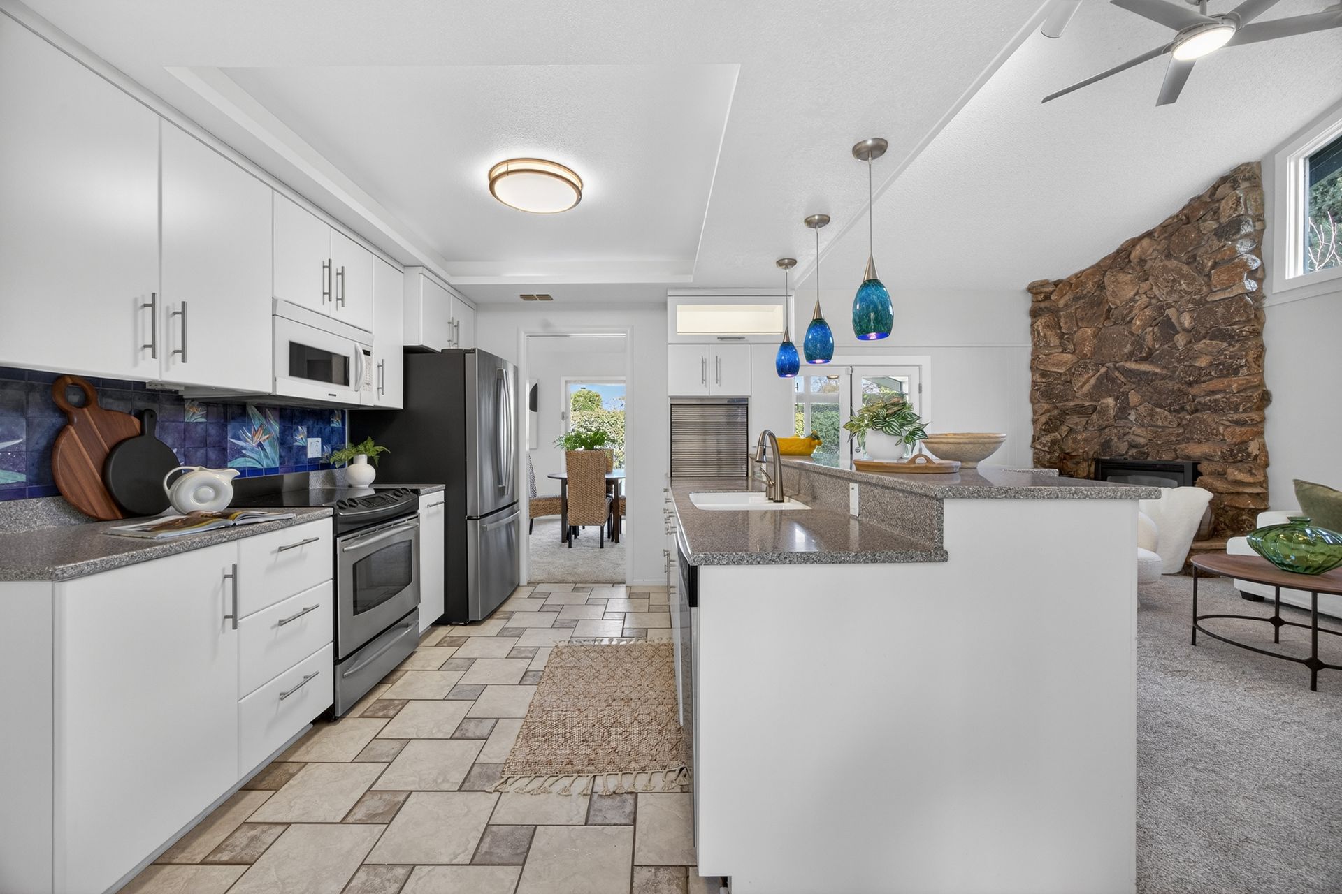 Modern kitchen with white cabinets, dark appliances, stone wall, and a central island.