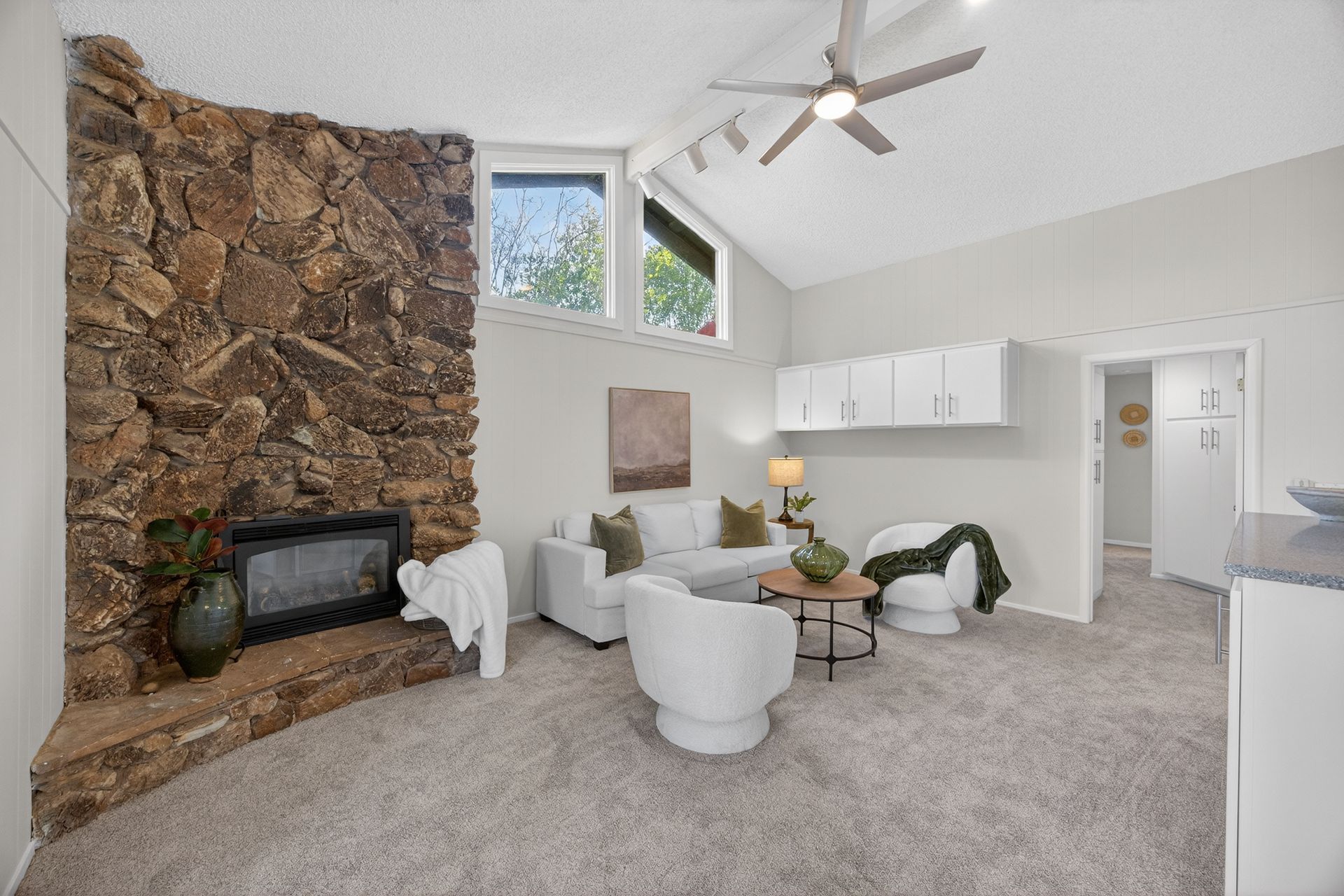 Living room with stone fireplace, white furniture, and gray carpet.