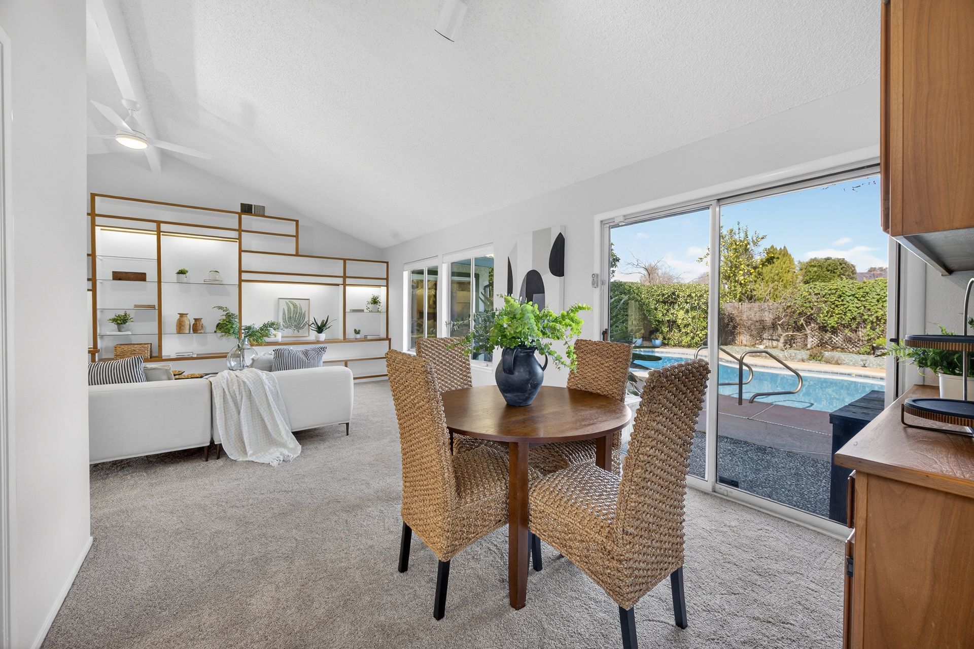 Dining area with table and chairs, sliding door to pool, living area with sofa and shelves.