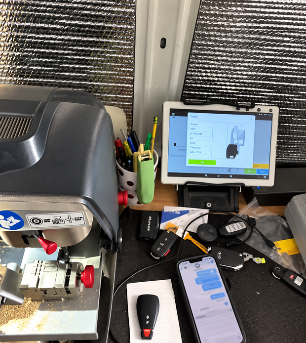 Cluttered workbench with a tablet, tools, wires, and a machine in front of a window.