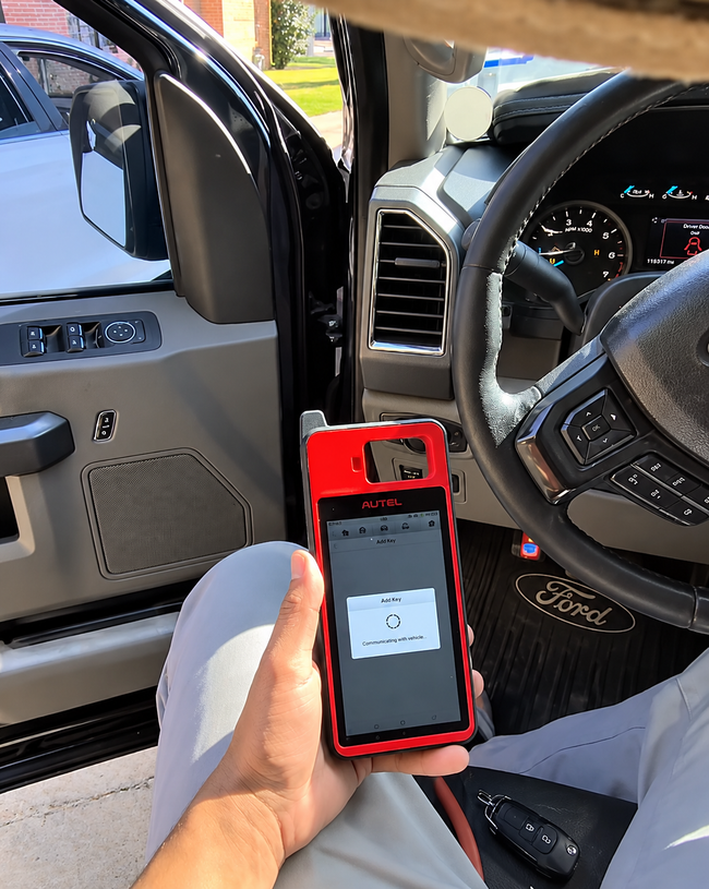 Hand holding a red smartphone inside a car, with the driver’s seat and steering wheel visible.