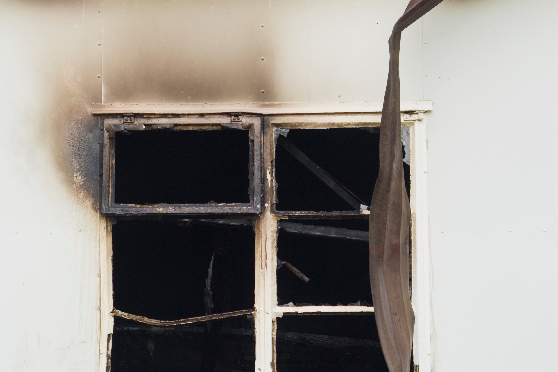 Burnt window on a white wall; interior fire damage with char and debris visible.