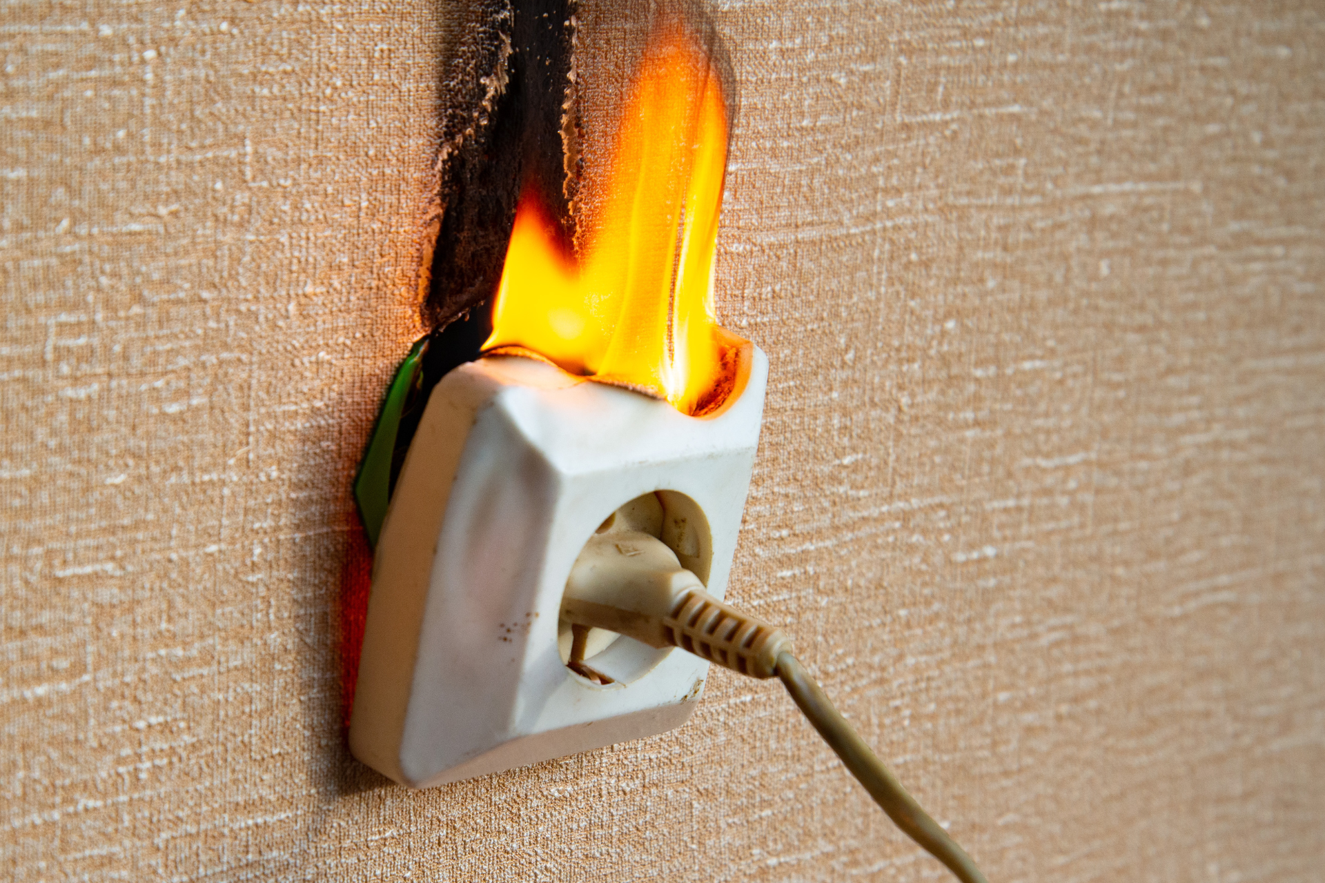 Burning electrical outlet with flames engulfing the surrounding wall.