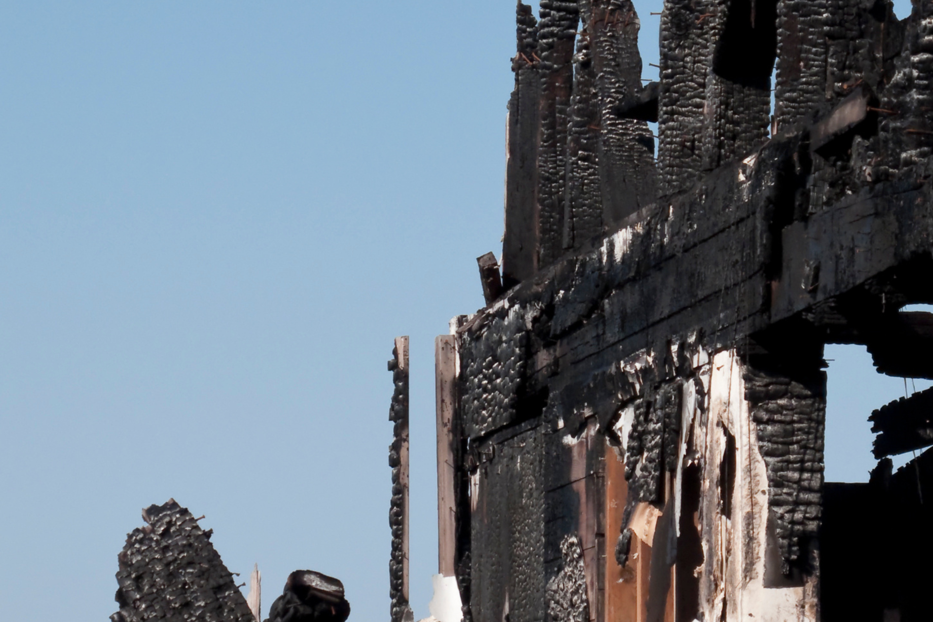 Charred remains of a building after a fire, against a clear blue sky.