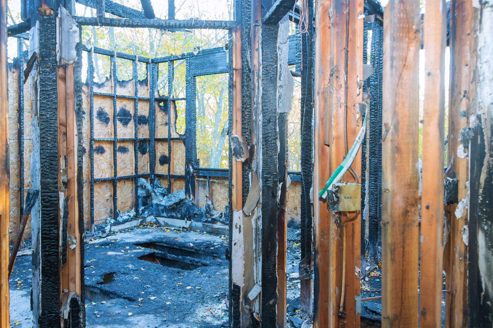 Charred interior of a building after a fire. Burnt wooden beams, walls, and a window frame are visible.