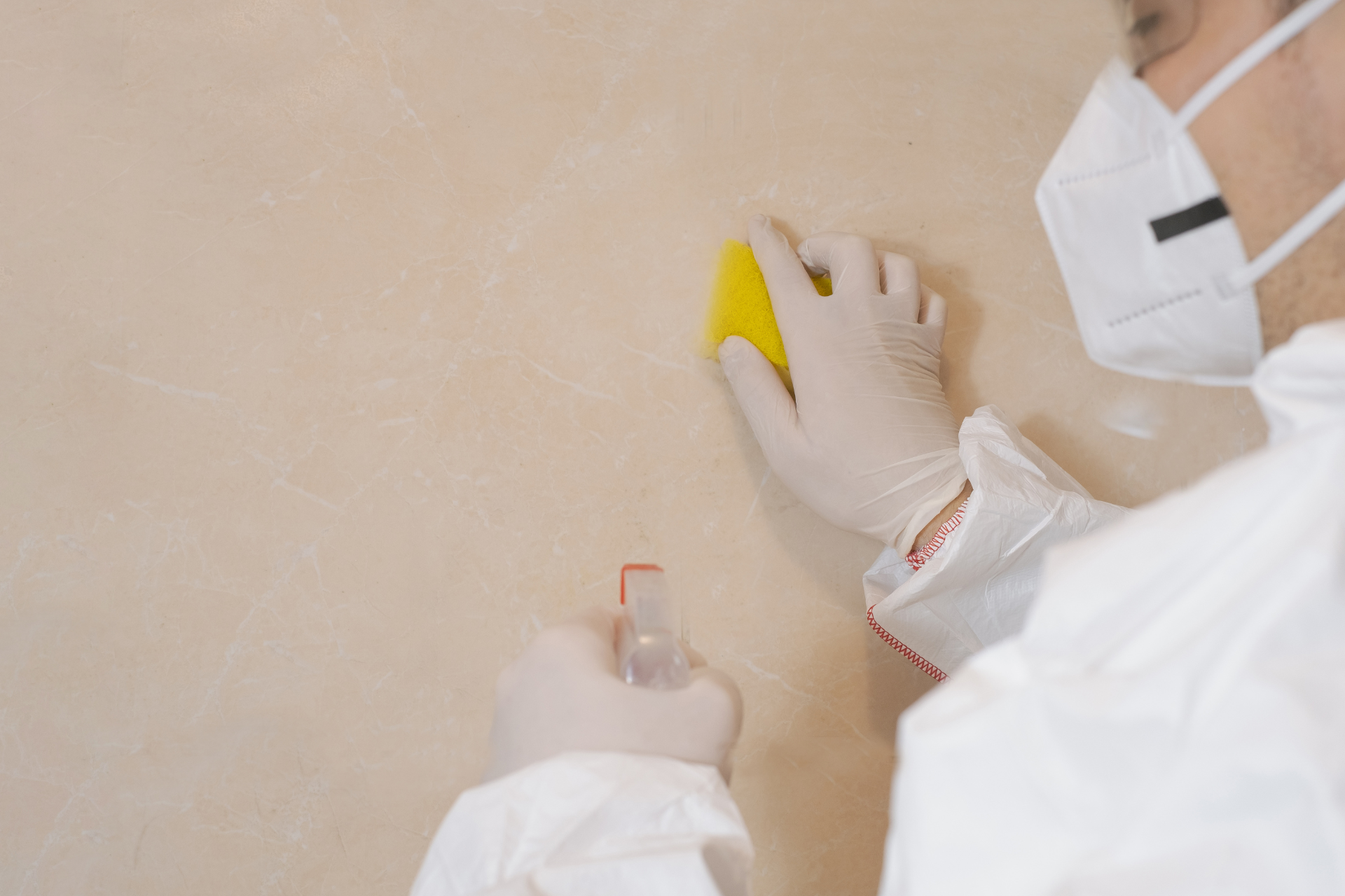 Person in protective gear cleaning a wall with a sponge and spray bottle.