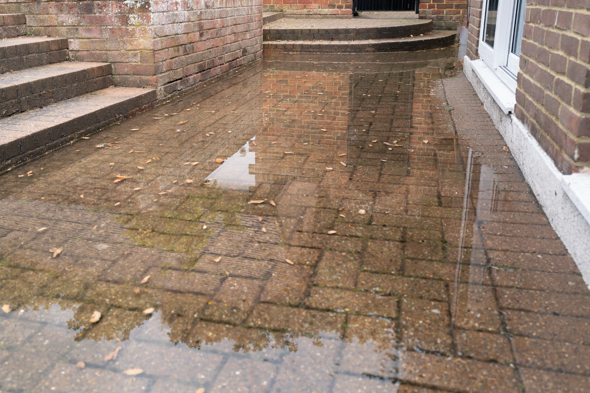 Flooded brick patio next to a brick wall and stairs, with water reflecting the buildings.