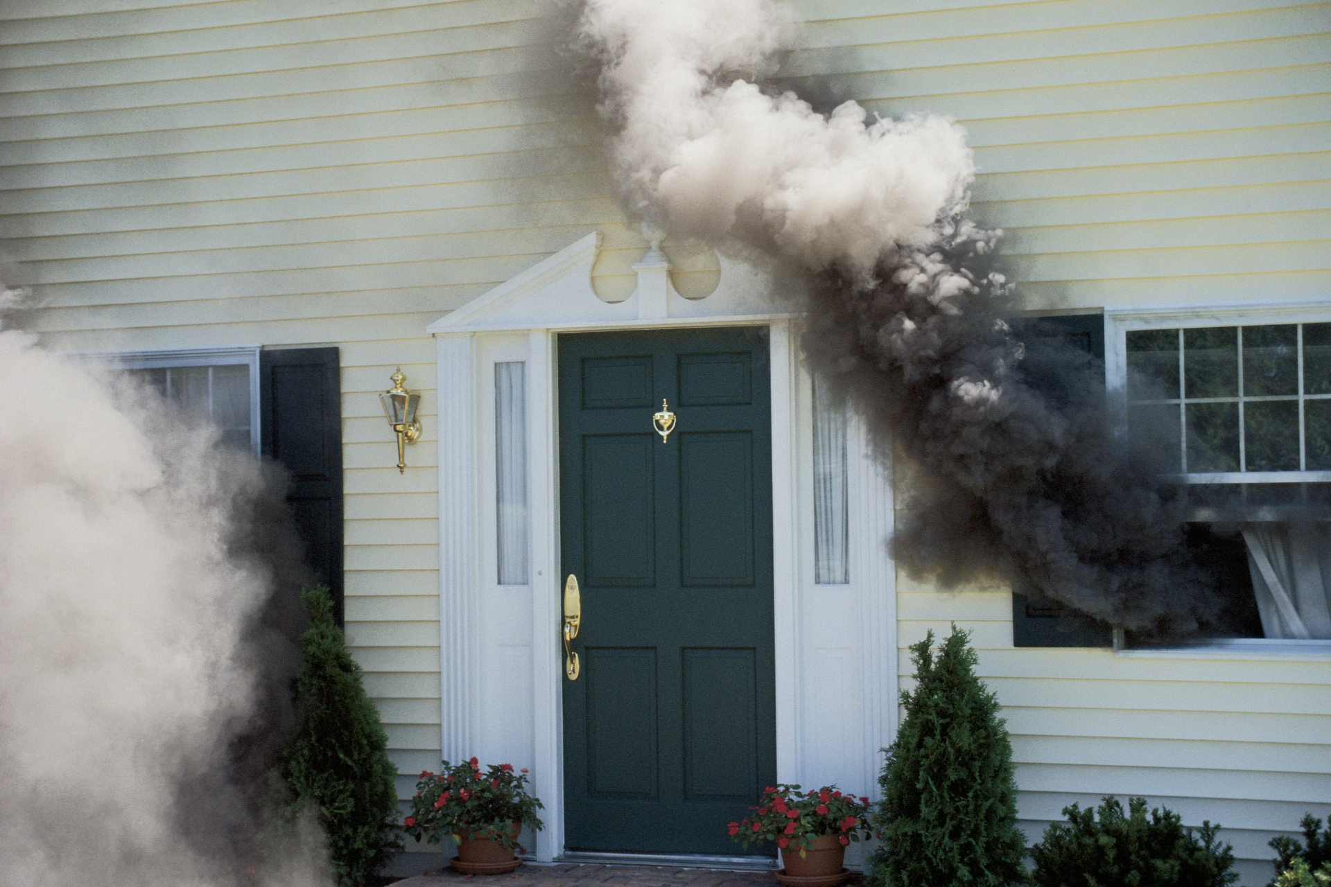 House with smoke billowing from windows and doorway, indicating a fire.