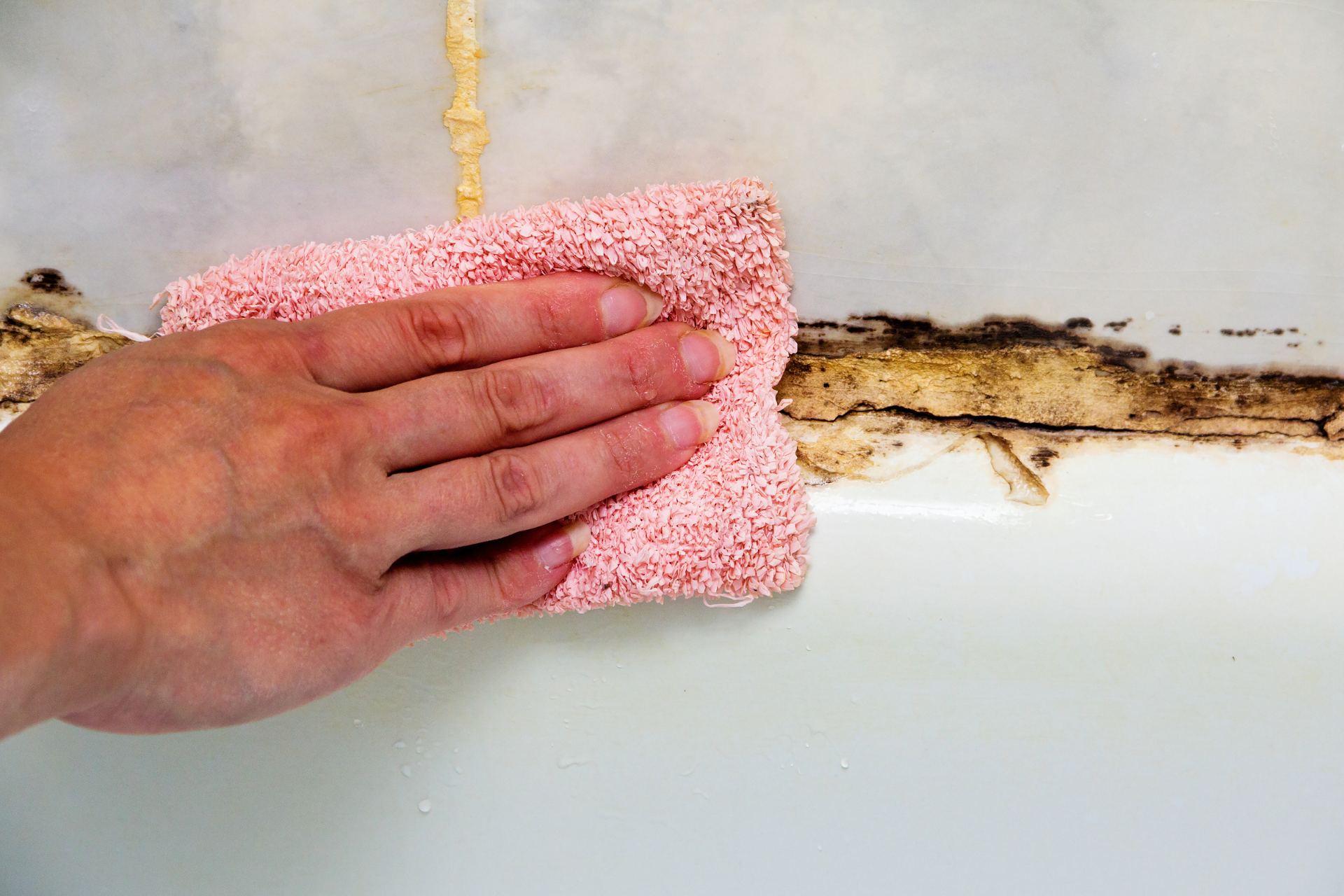 Hand scrubbing moldy tile grout with a pink cloth in a bathroom.