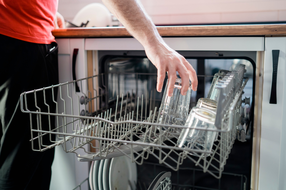 Person loading glasses into a dishwasher.