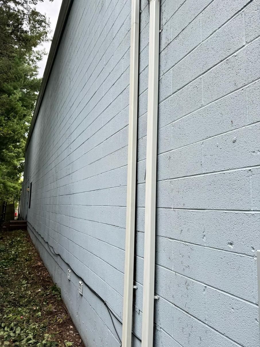 A gray brick wall with a white pipe on the side of it.