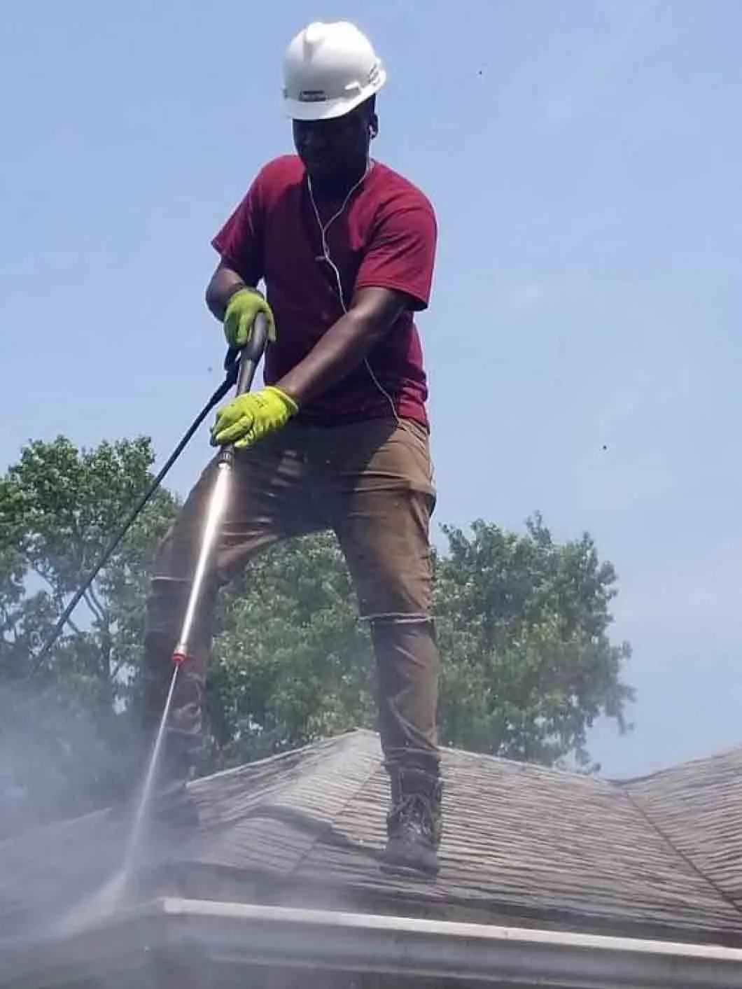 A man is cleaning the roof of a house with a high pressure washer.