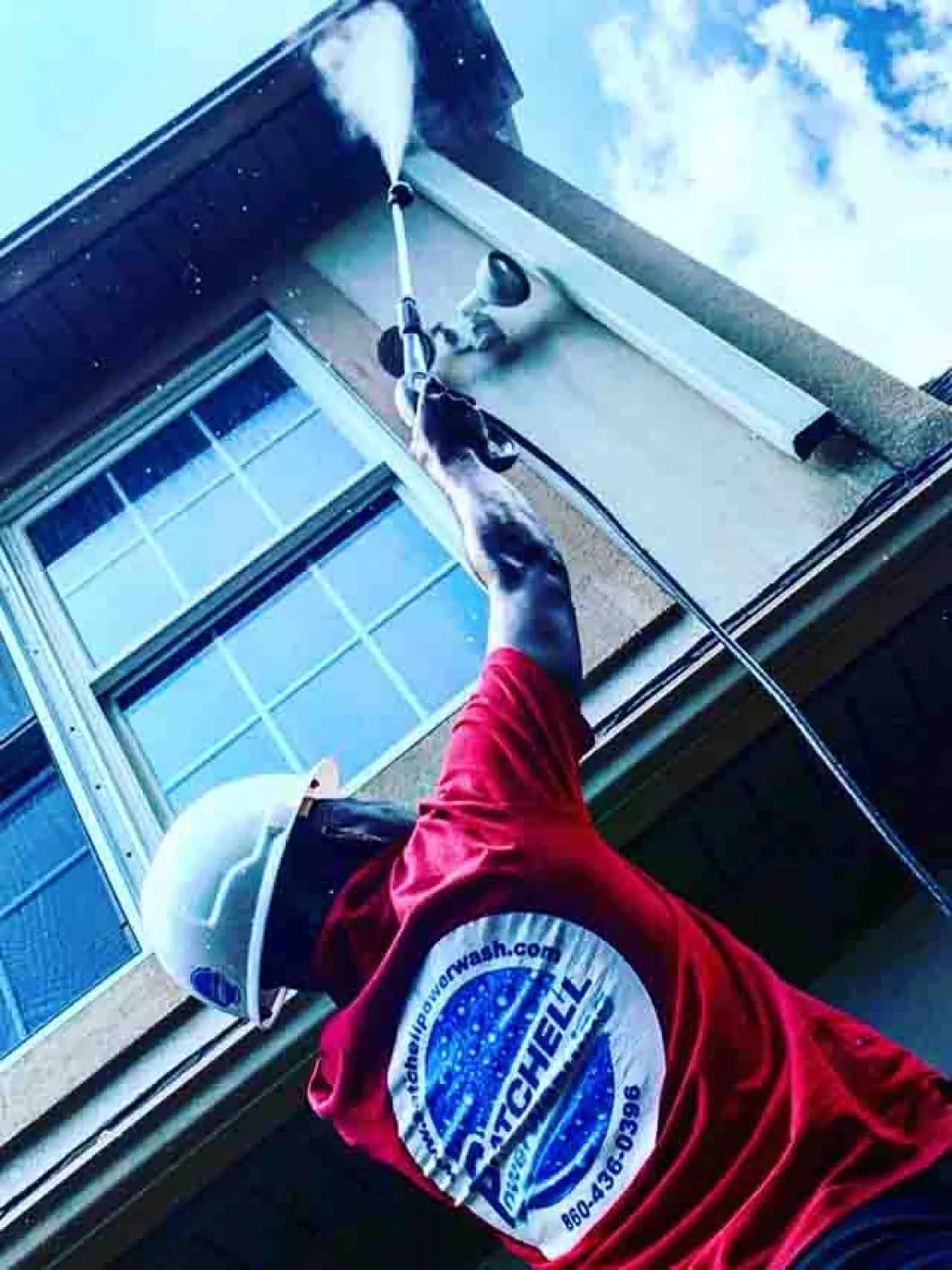 A man in a red shirt is cleaning the side of a building with a pressure washer.