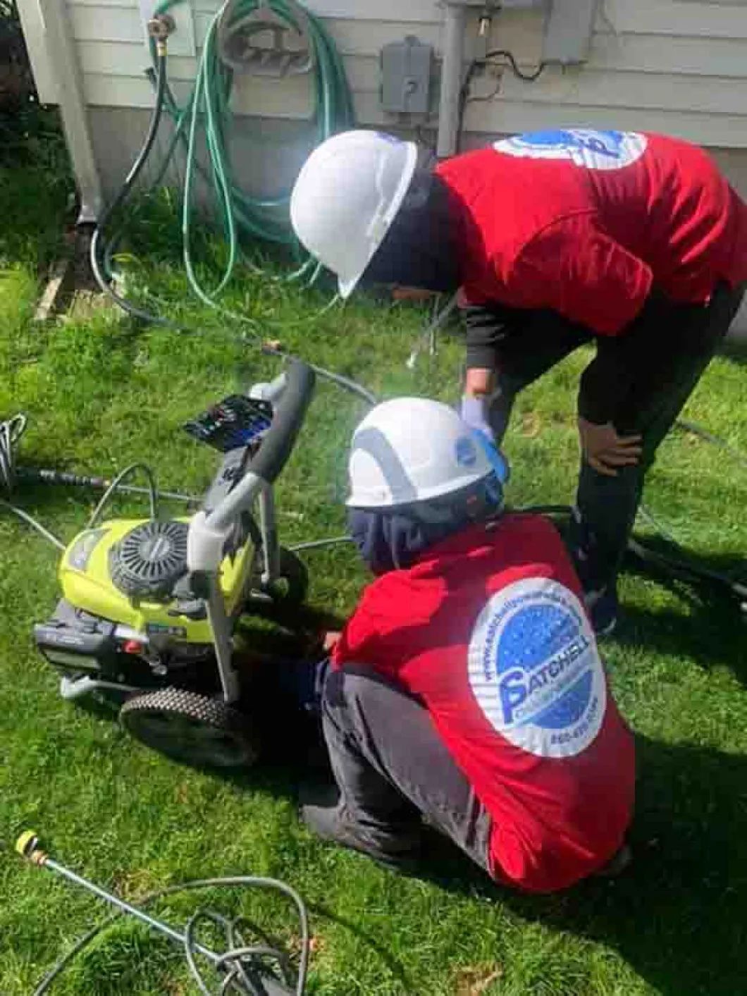 Two men are working on a pressure washer in a yard.