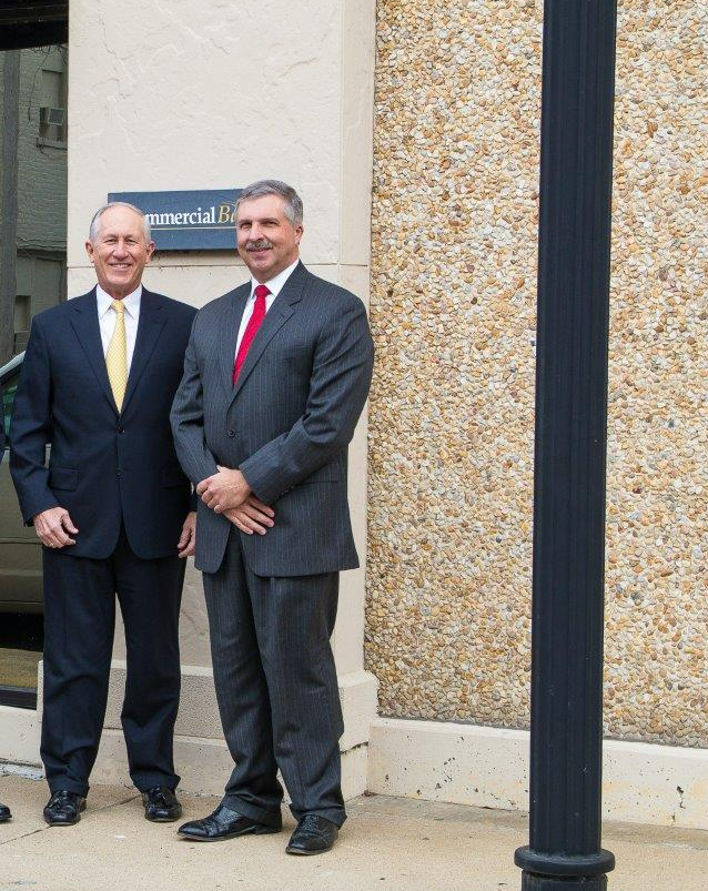 Two men in suits standing outside a building with a sign that reads