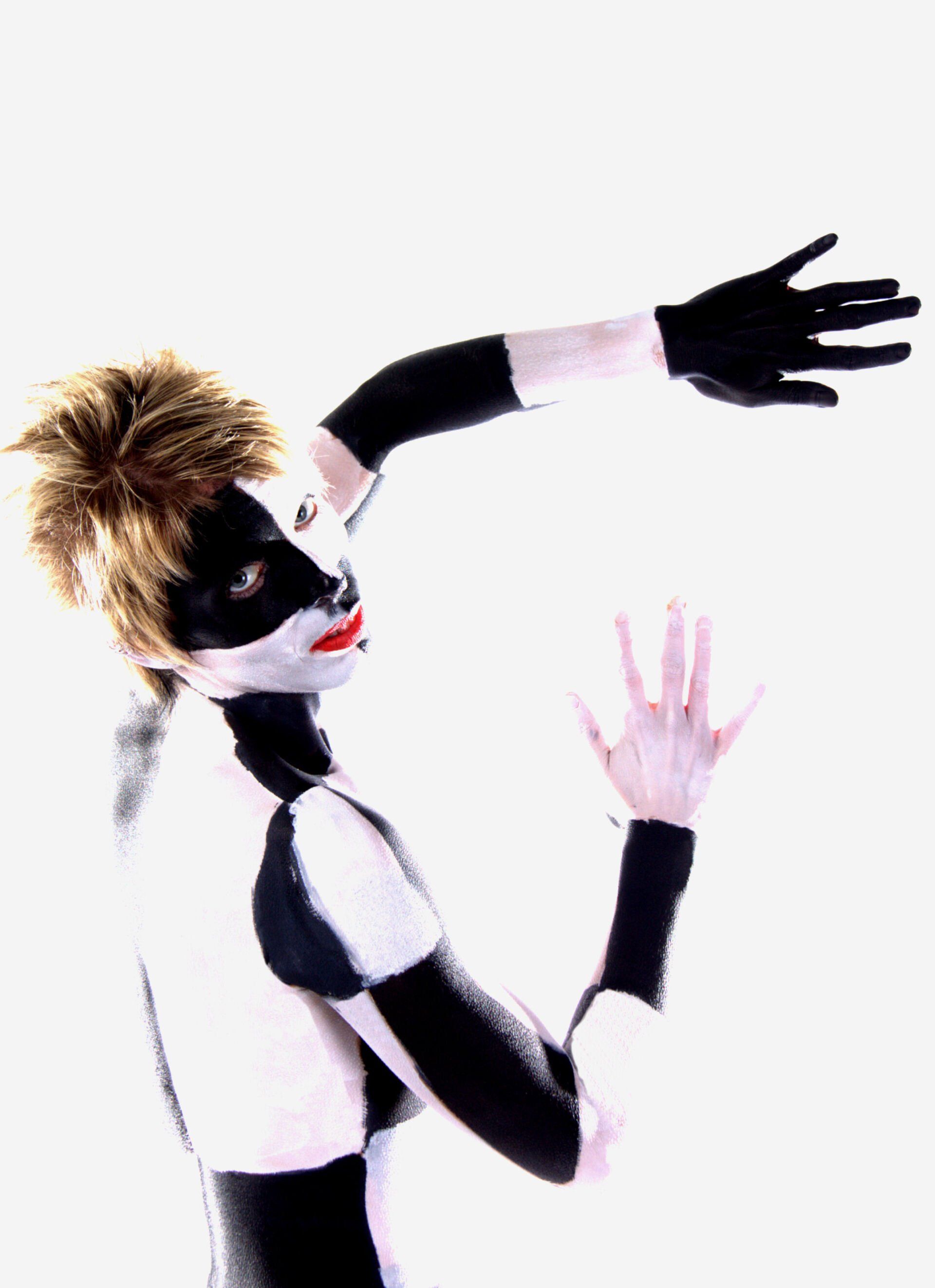 Persoon met zwart-witte bodypaint en handschoenen poseert tegen een witte achtergrond.