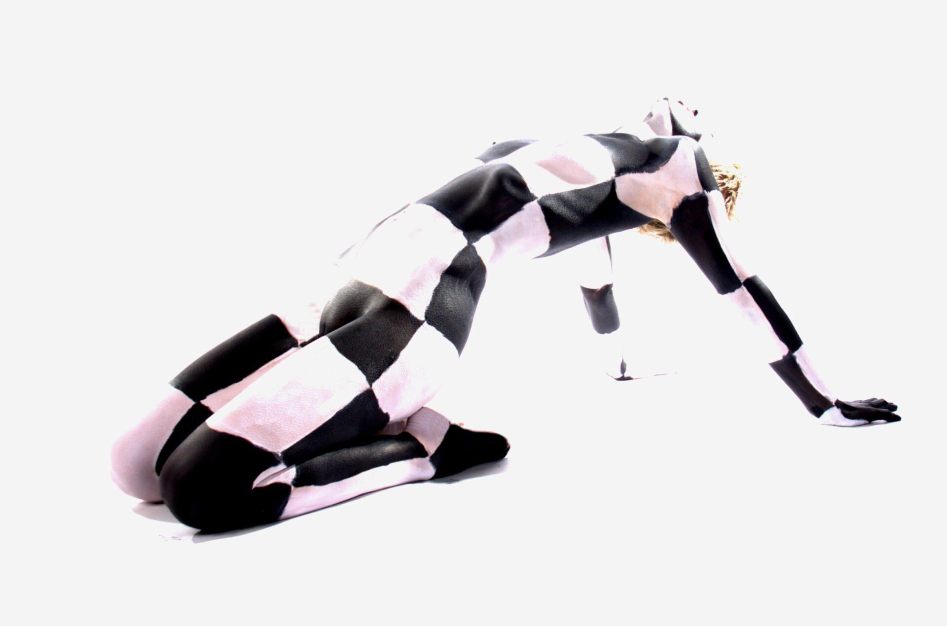 Abstracte zwart-wit geblokte figuur die op handen en knieën kruipt tegen een witte achtergrond.