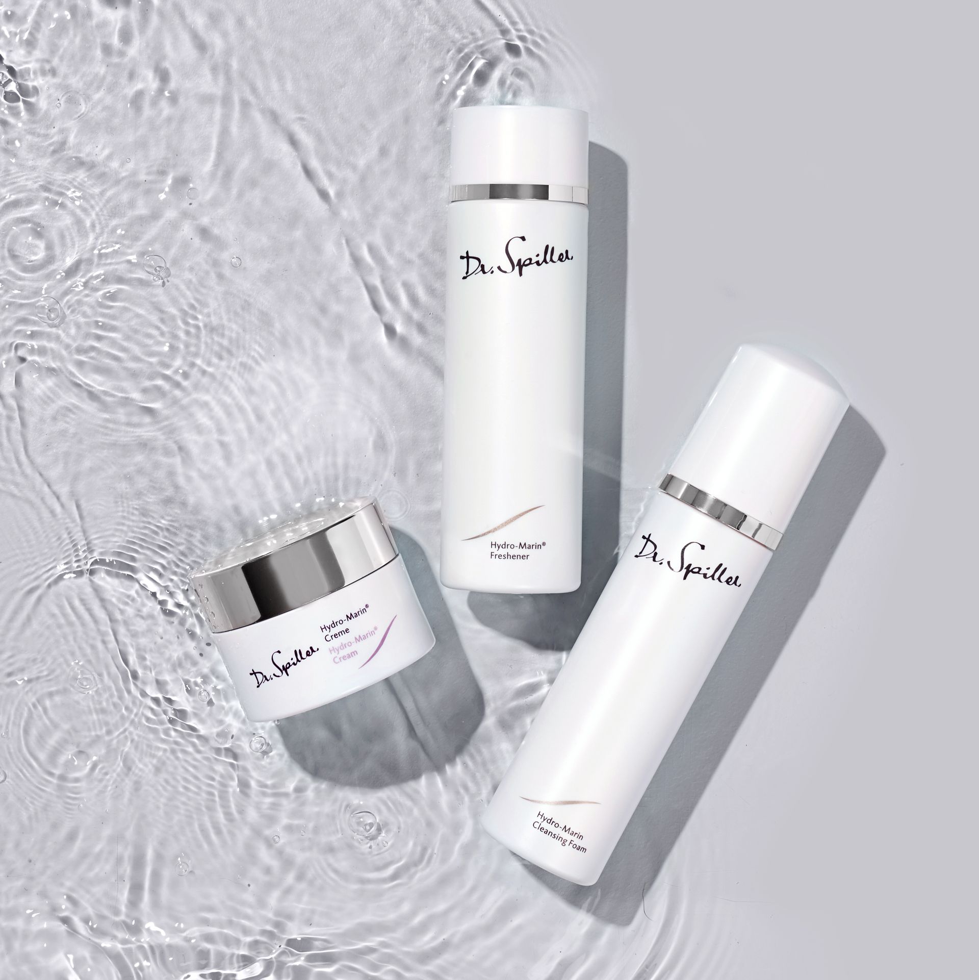 Three white cosmetic bottles and a jar on a textured gray background.
