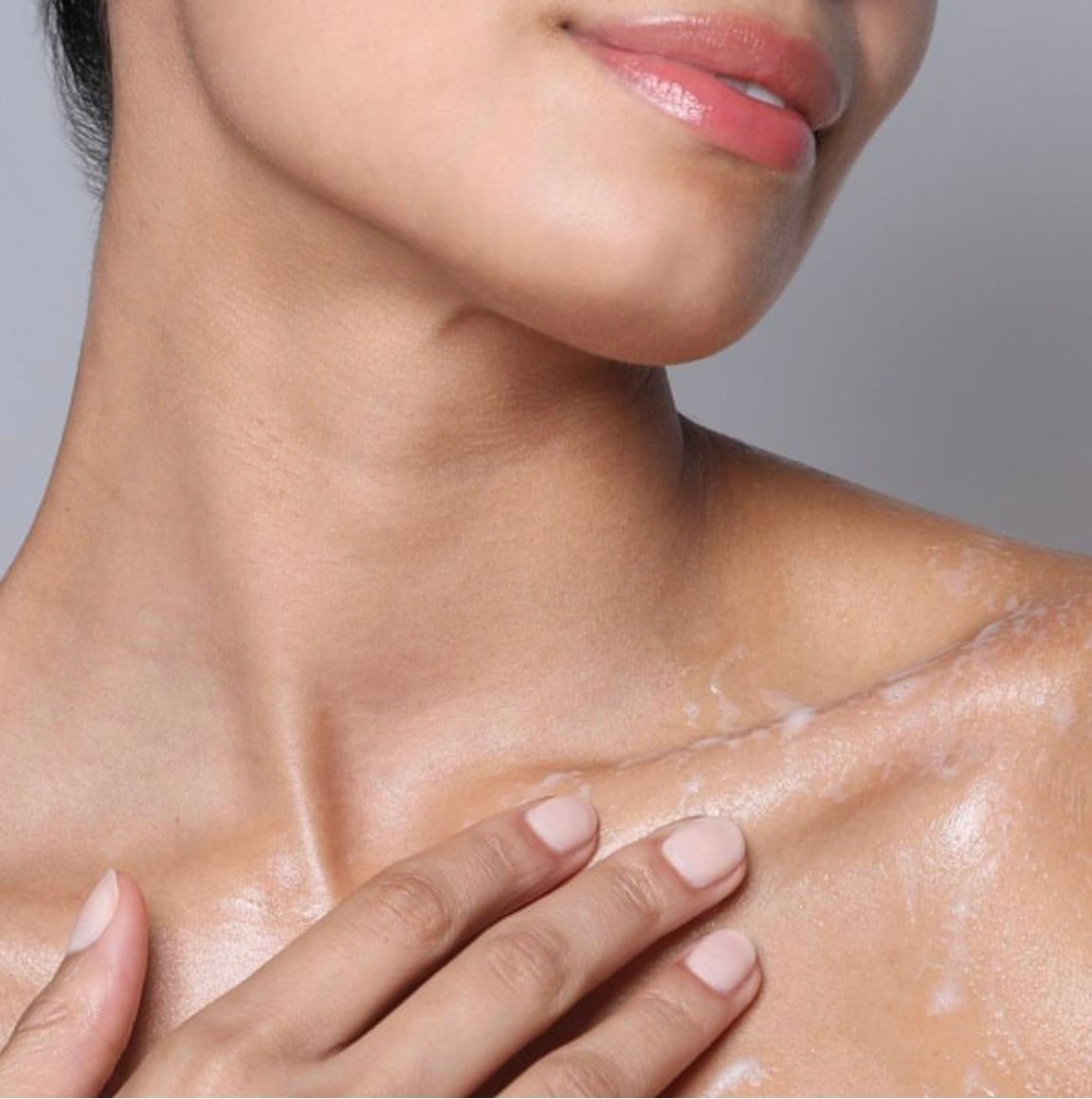 Close-up of a person touching a shiny shoulder and neck with soft pink lips visible