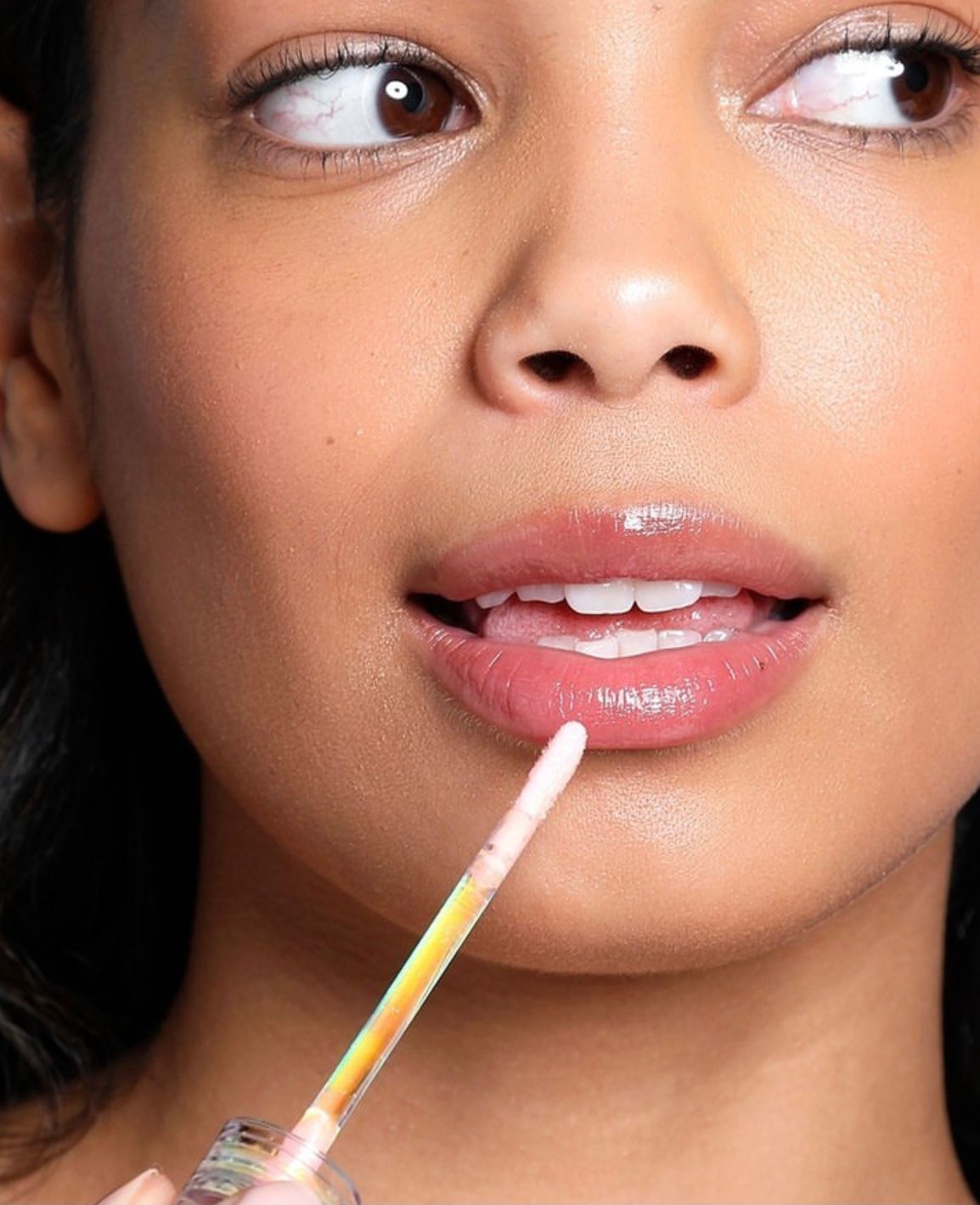 Close-up of a person applying clear lip gloss with a wand, lips slightly parted
