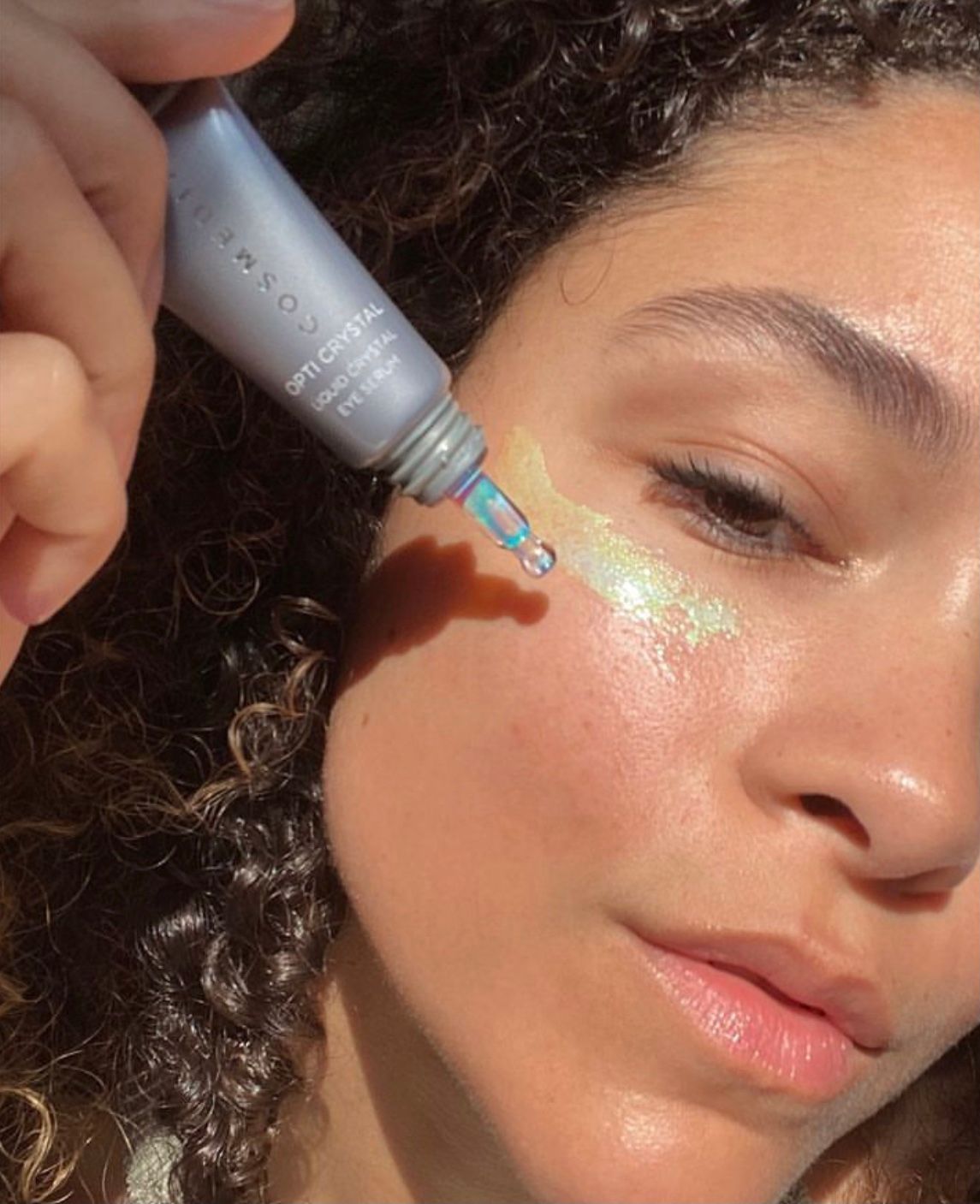 Close-up of a person applying shimmering cream under one eye with a tube applicator.